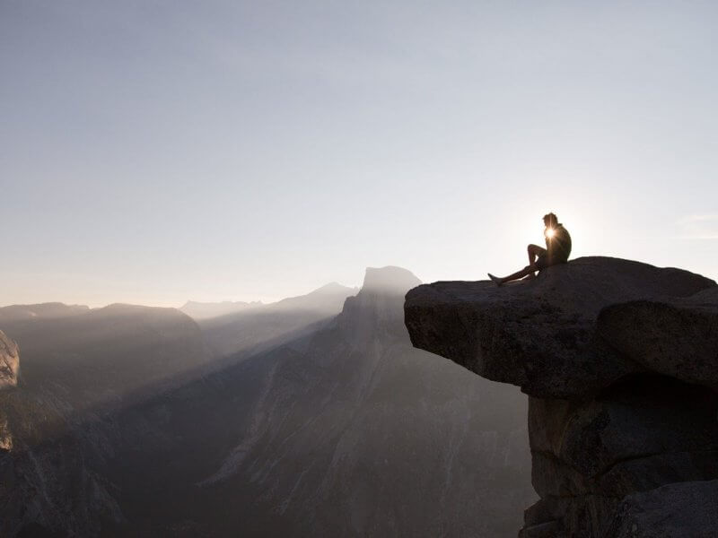 Ein Mann der auf einer Klippe sitzt und den Sonnenaufgang genießt. Er hat seinen Beruf gefunden.