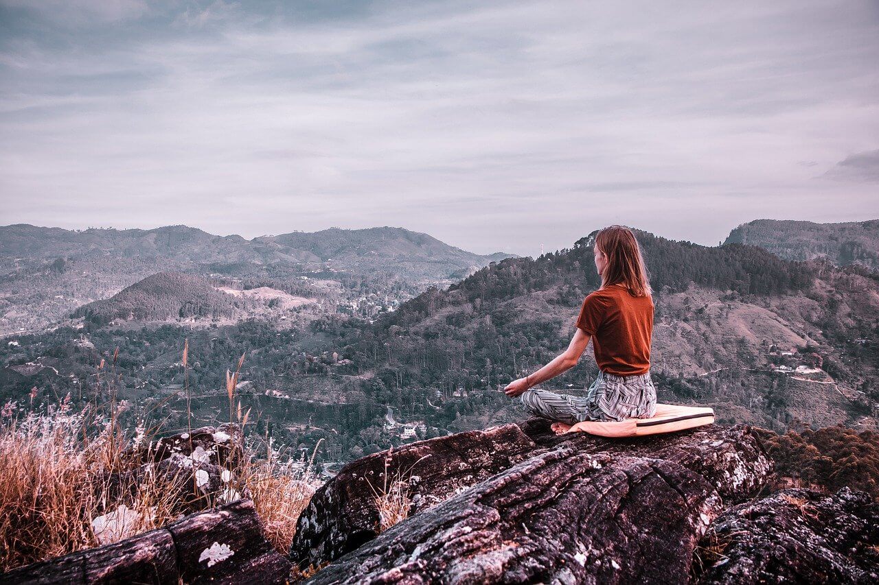 Selbstverwirklichung durch Meditieren. Frau sitzt in den Bergen und meditiert.
